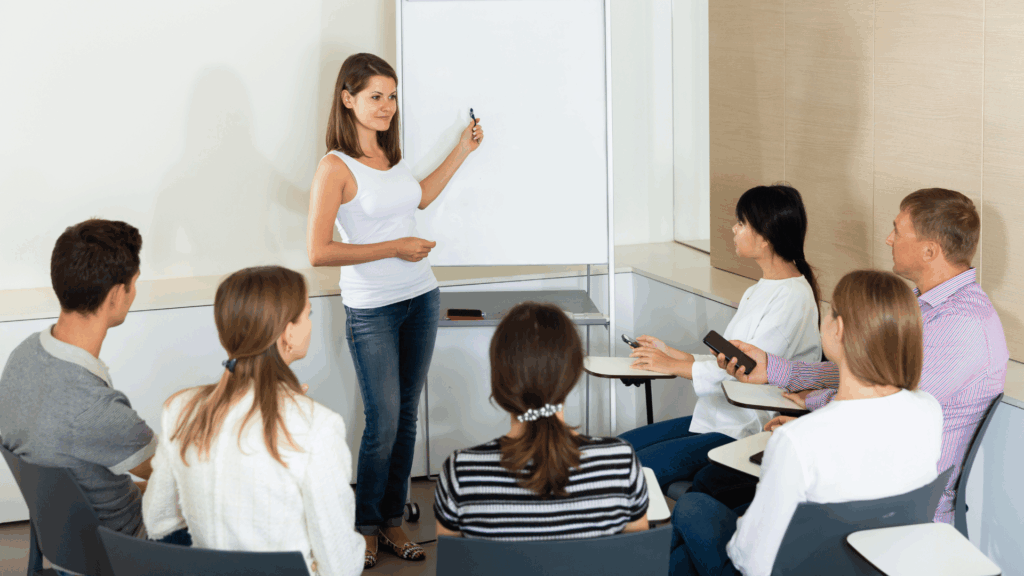 Femme debout présente un tableau blanc à ses 6 collègues