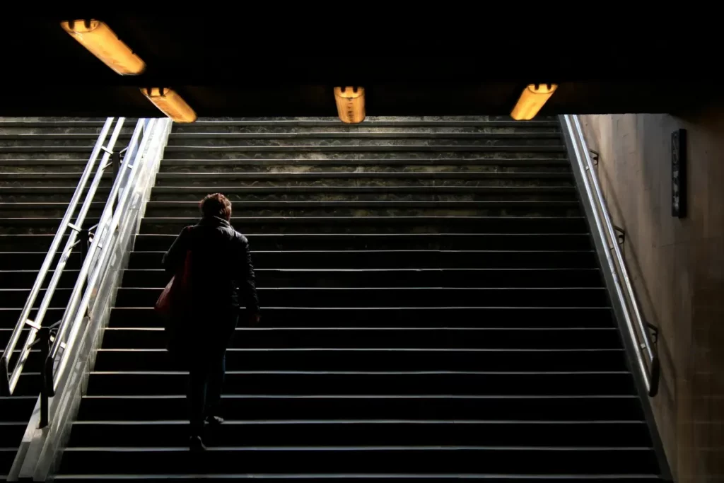 Individu montant un escalier souterrain, dans un métro, symbolisant le dur labeur et l'espoir